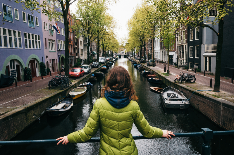 Young woman stands on the bridge and looks at the canal of Amsterdam, Netherlands