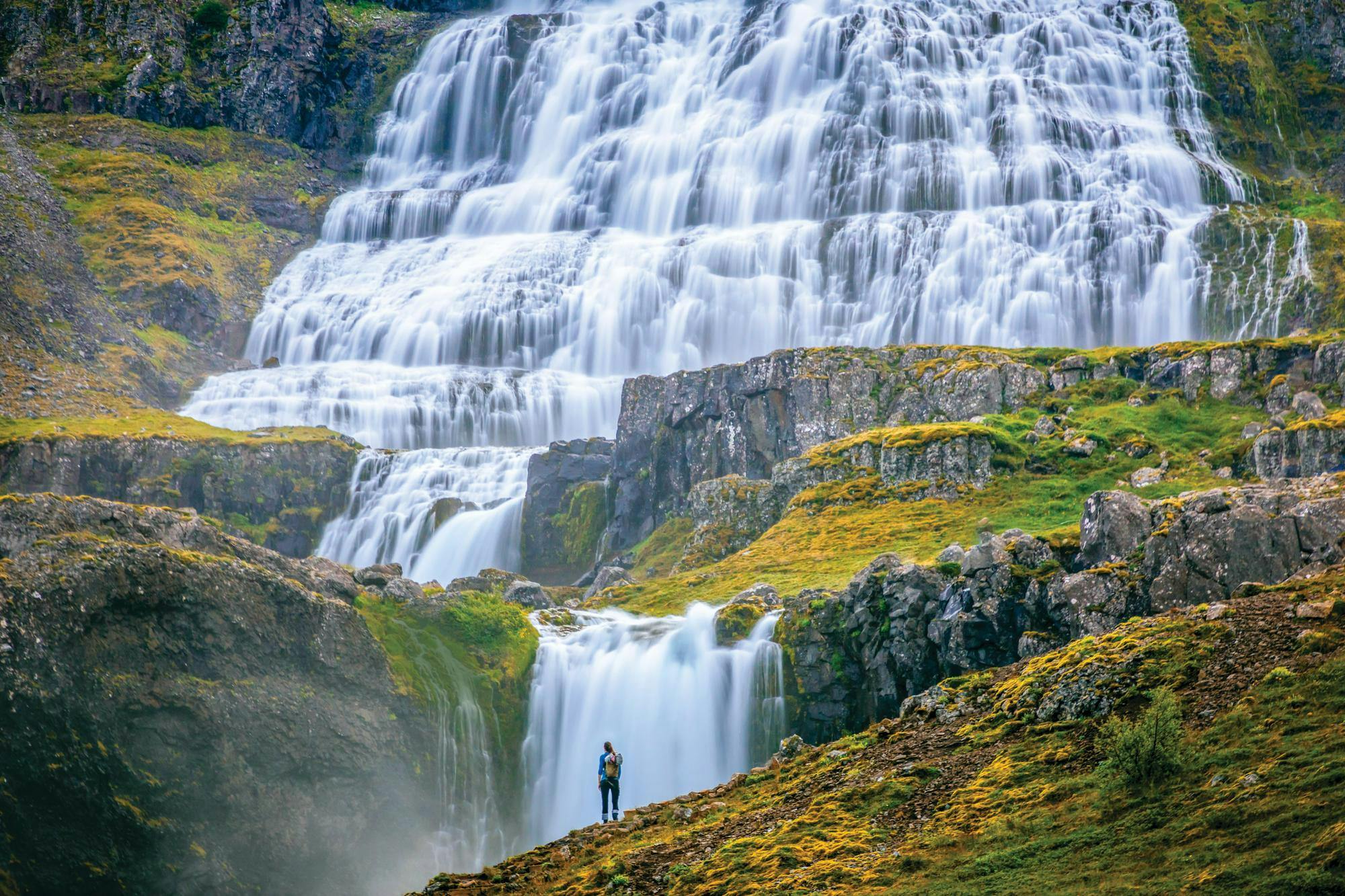 A hiker stands in front of the Dynjandi waterfall in Arnarfjörður in the Westfjords region of Iceland
