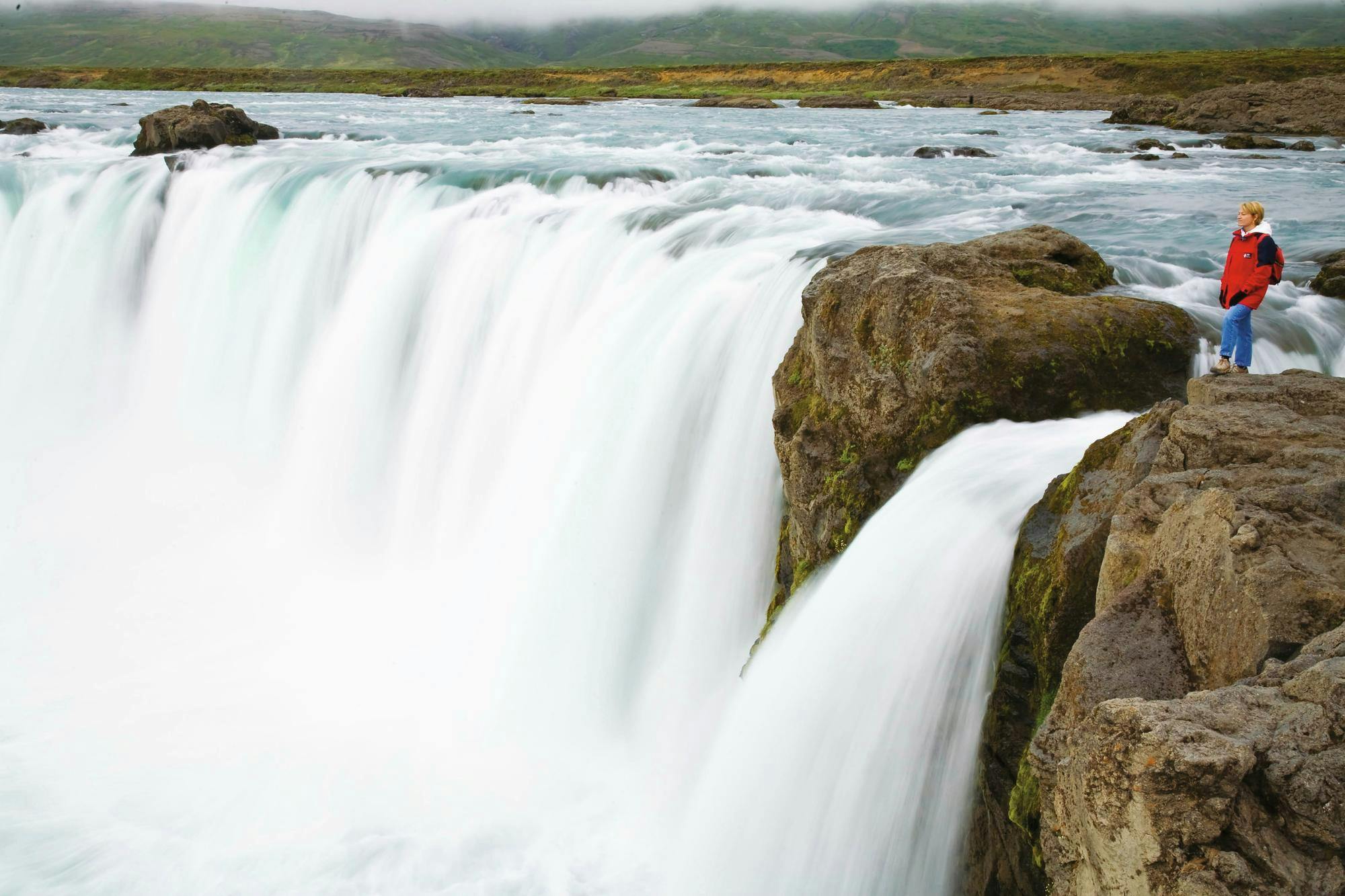 A guest hikes at the top of Goðafoss, the waterfall of the gods, off the north coast of Iceland