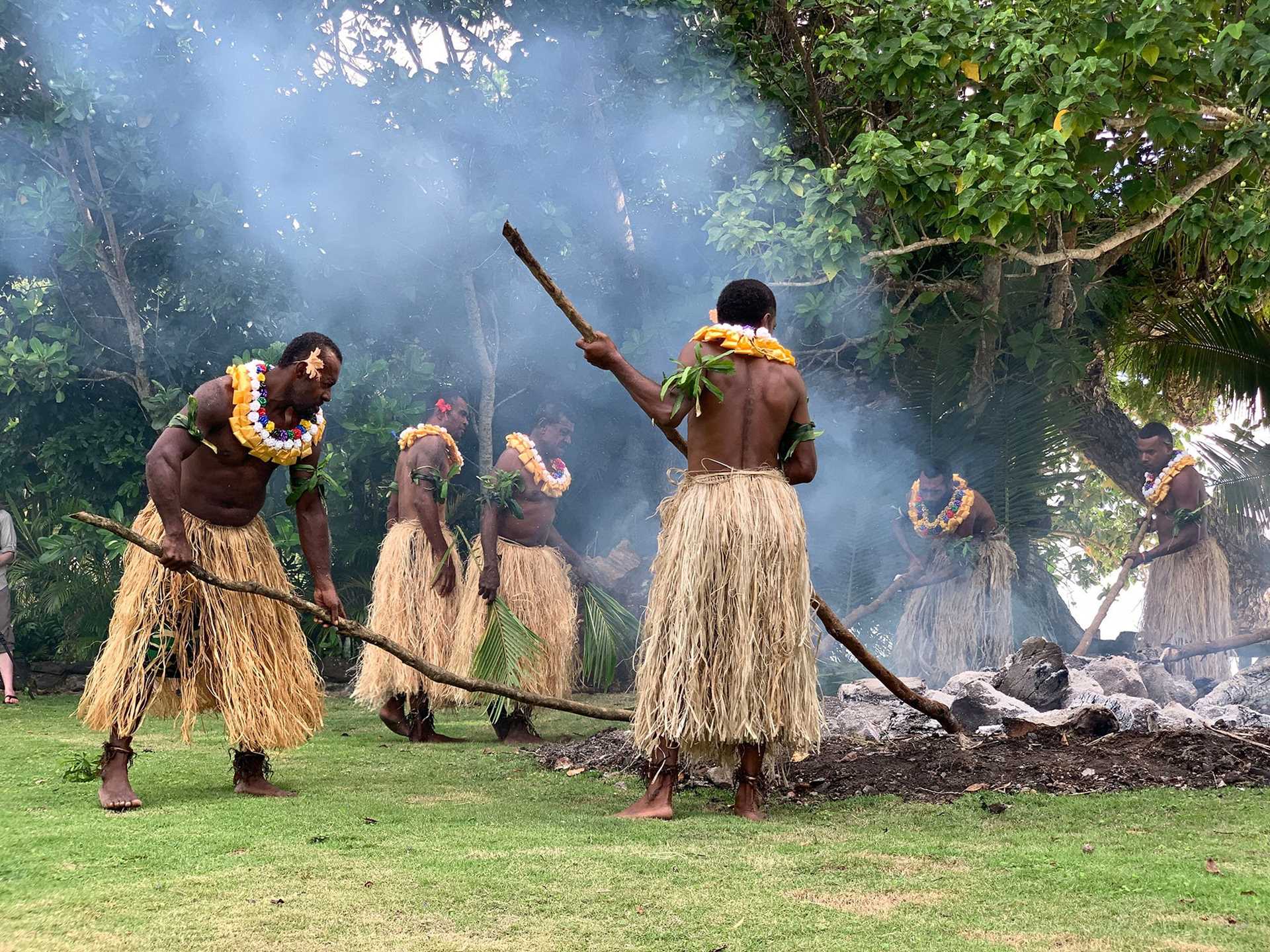 men in grass skirts prepare hot coals for firewalking