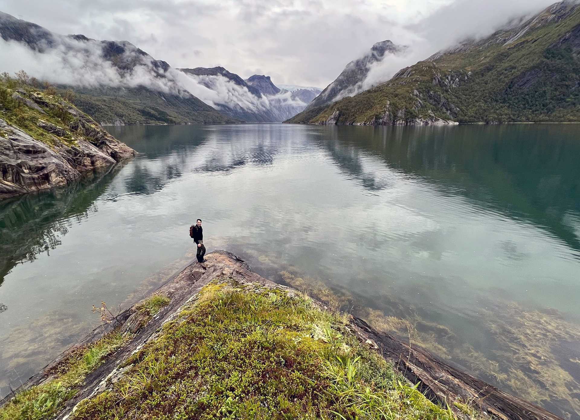 hiker standing on a bank in front of a fjord