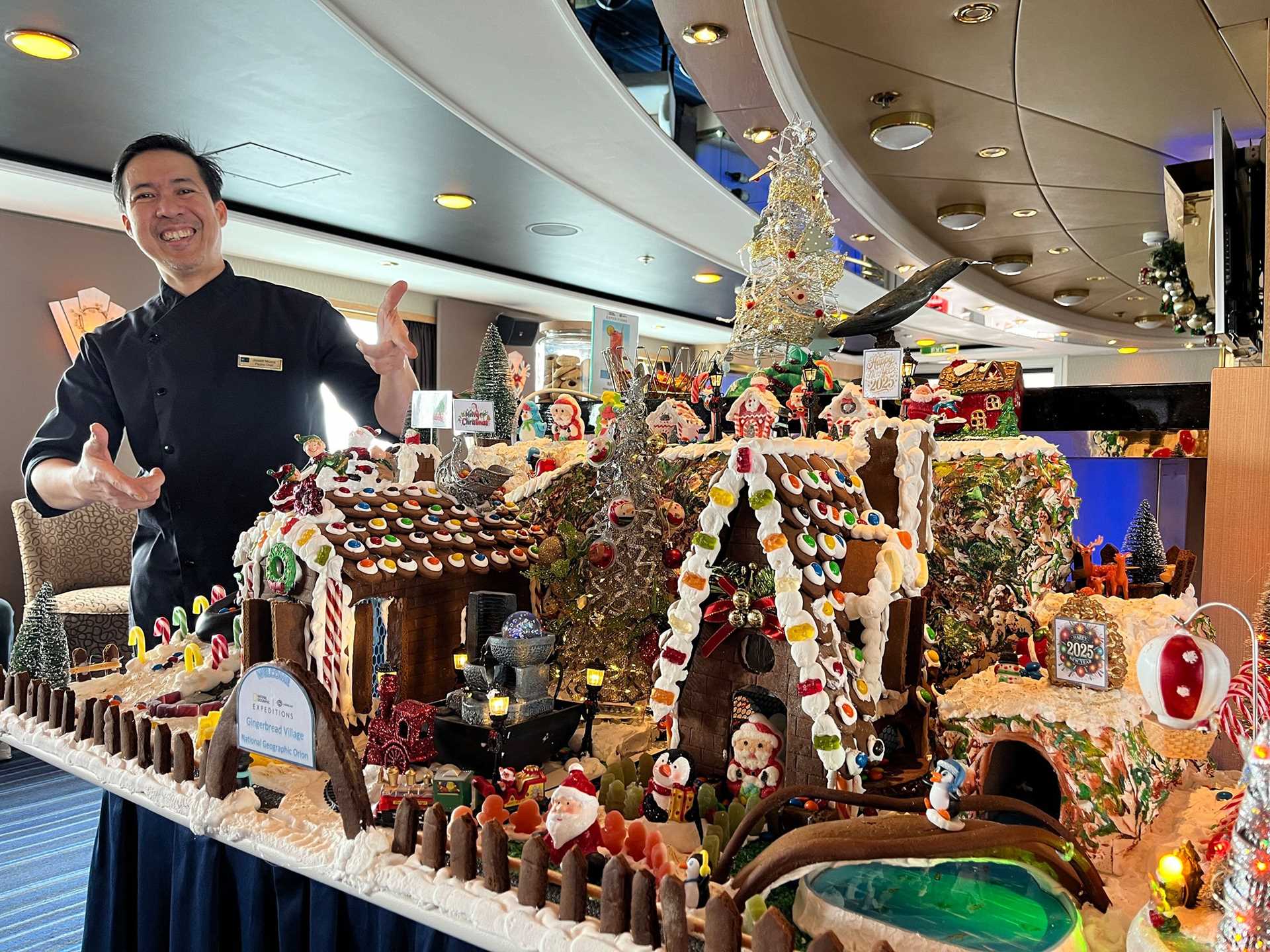 a man stands next to an elaborate gingerbread house