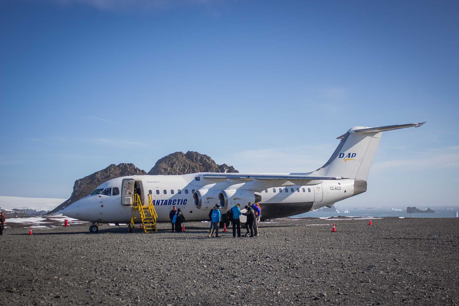 Travelers stand outside a plane on a runway in Antarctica.