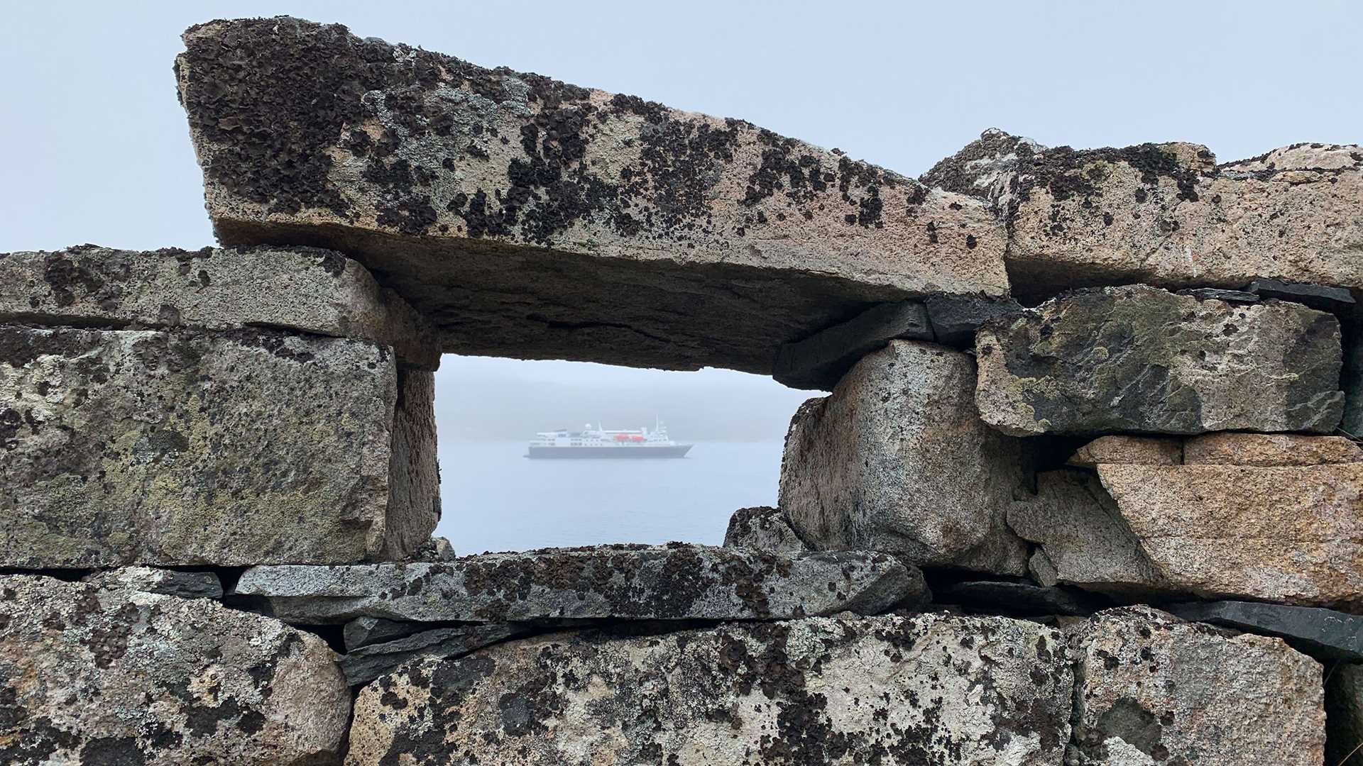 ship seen through a hole in a rock wall