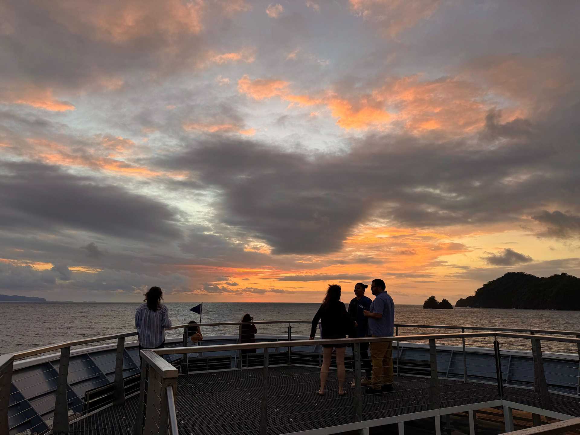 people stand on the deck of National Geographic Quest at sunset