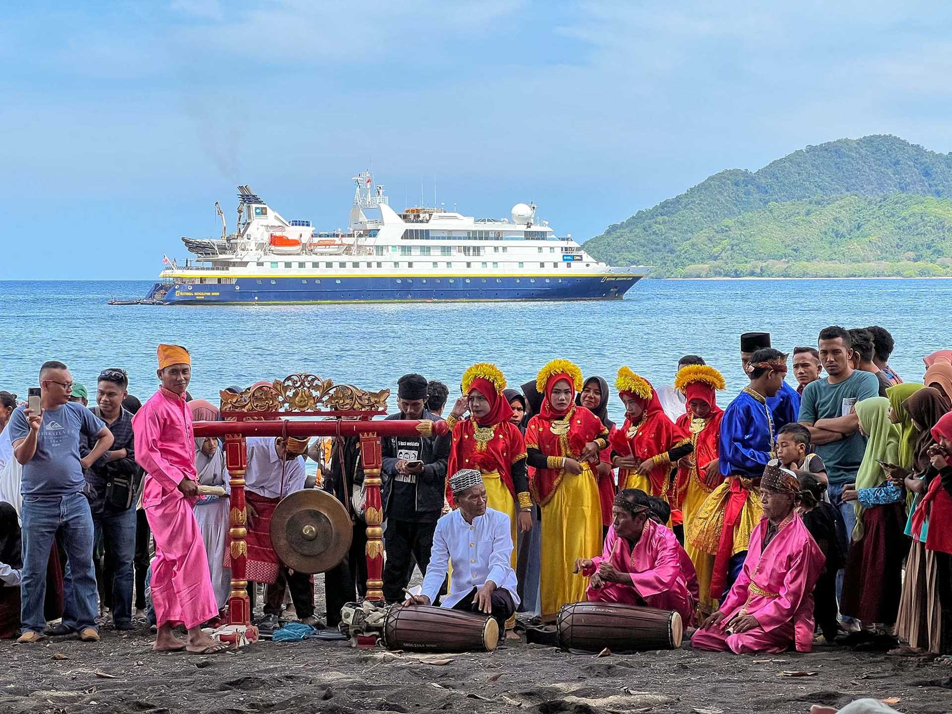 indonesian locals standing on the beach looking at national geographic orion ship