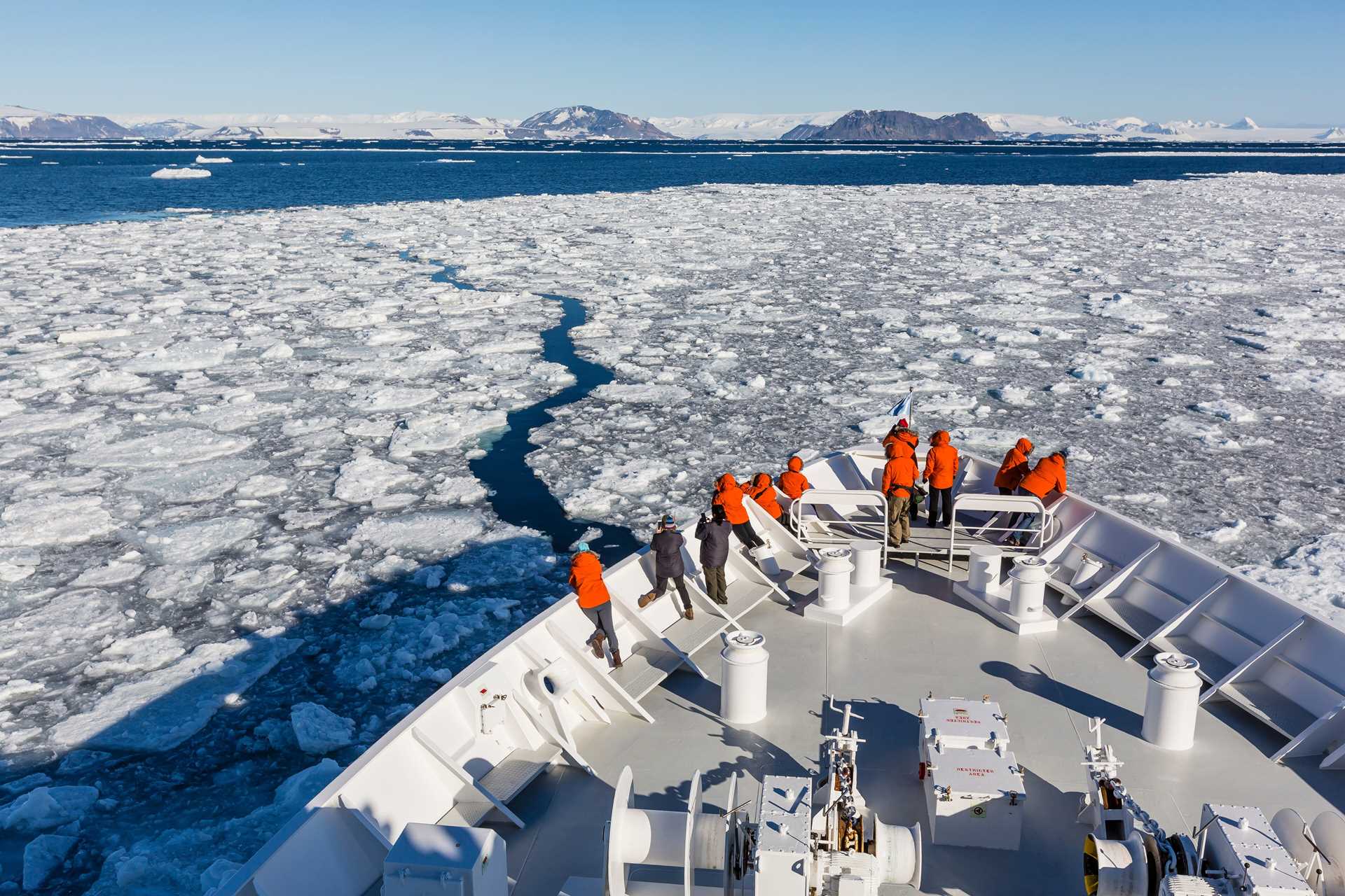 Guests stand on the bow of the National Geographic Orion as it sails through ice in Antarctica.