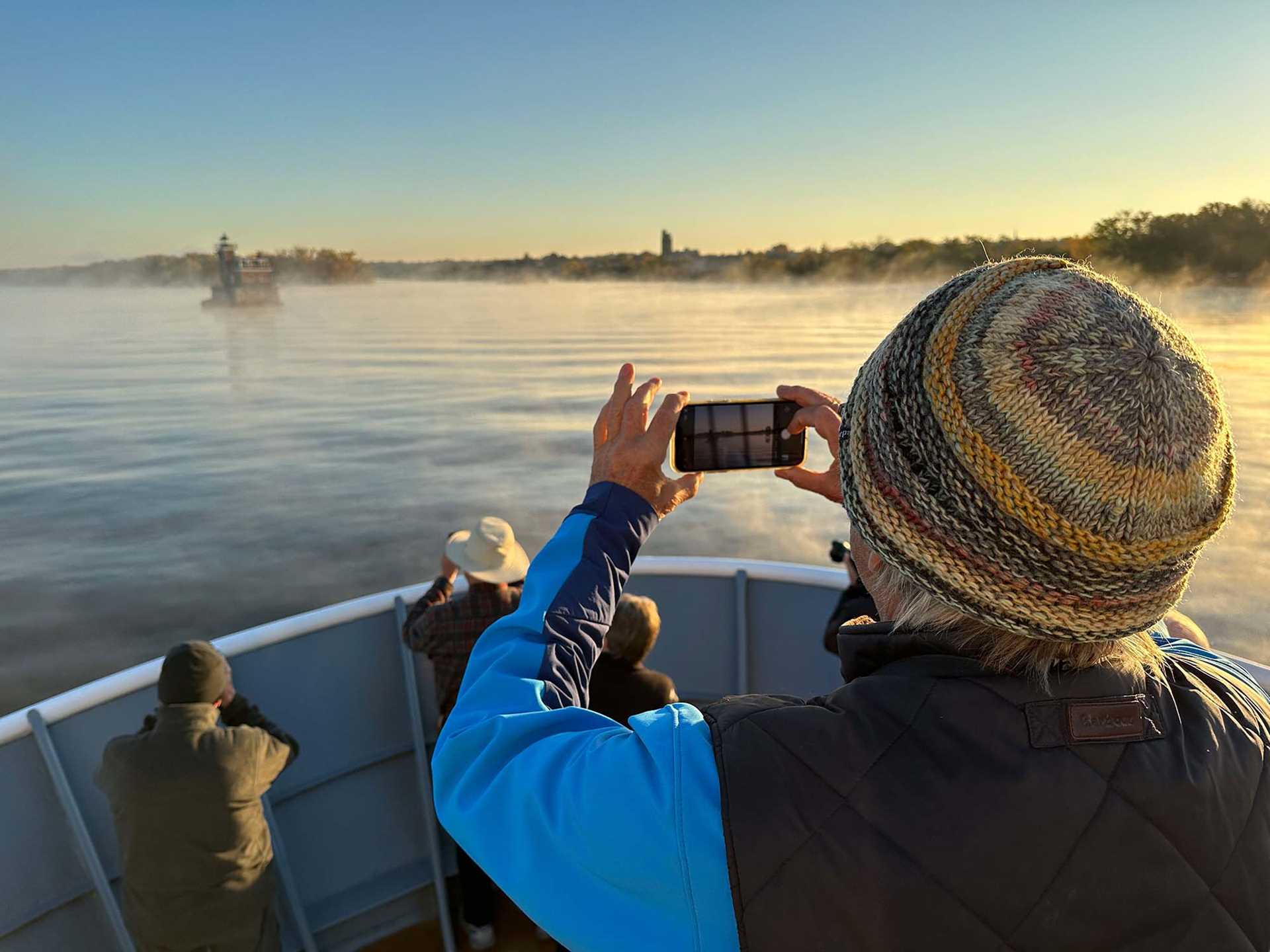 photographer on the deck of a ship, taking a photo of a lighthouse