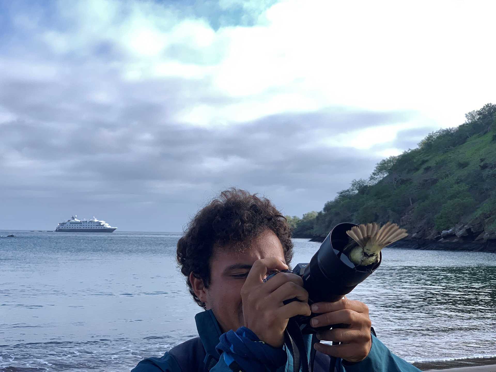 a man holds a camera while a bird attempts to climb inside the lens