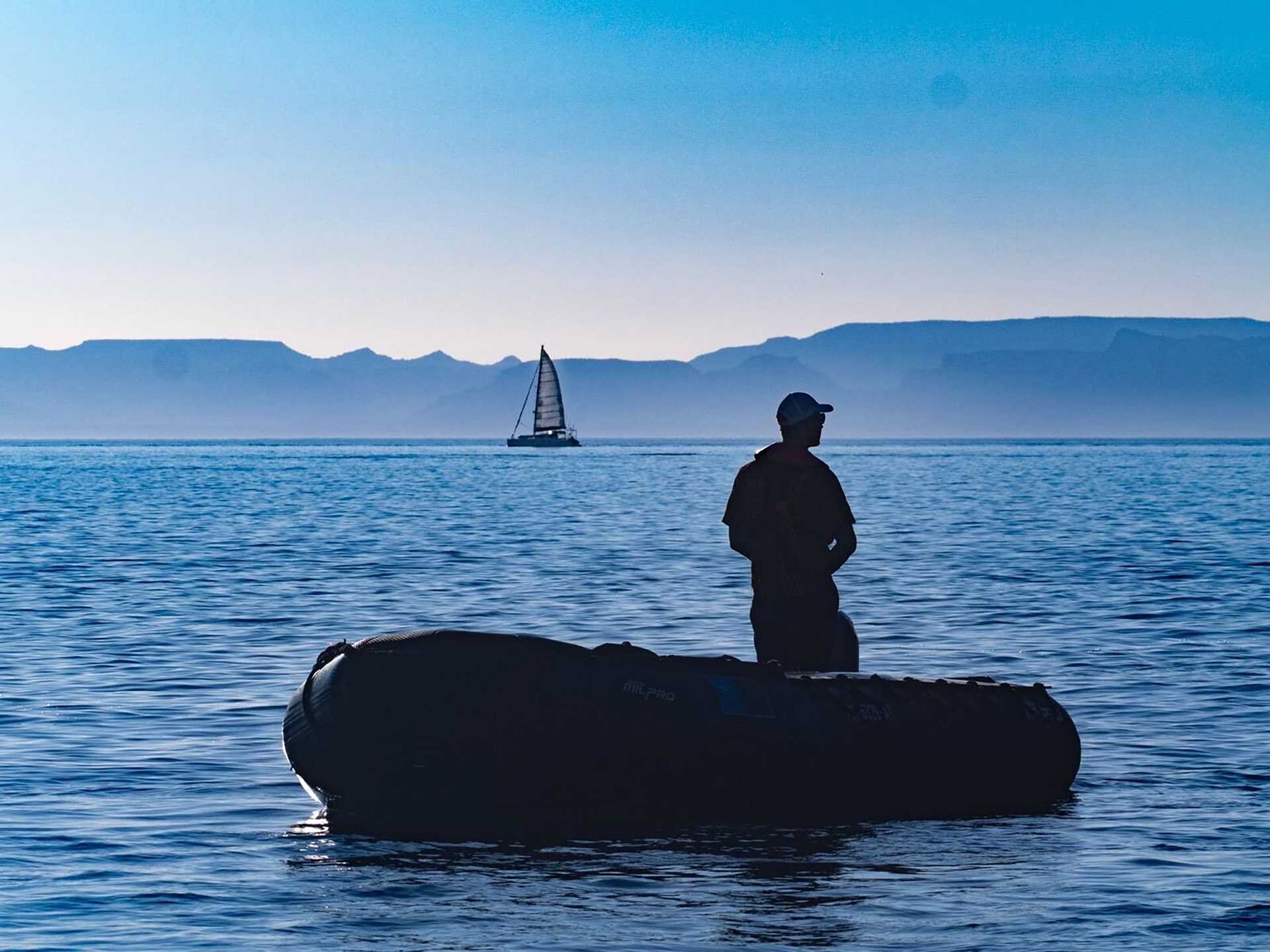 a man in a zodiac craft silhouetted against the sunset